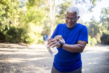 Older adult wearing a blue shirt and a fitness watch holding a bottle of water and getting out into the morning sunlight for stronger, healthy bones