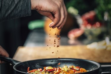 Sprinkling Ground Red Chili Pepper over Sliced Vegetables, as an example of spicy food that makes you sweat