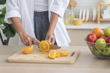 Person chopping oranges on wooden cutting board to get vitamins to boost metabolism and vitamins that help you lose weight