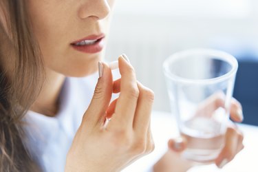 a closeup of an adult holding a pill and a glass of water