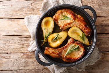 Rustic style baked pork chops with pears and rosemary in honey-garlic sauce served in a pan close-up.