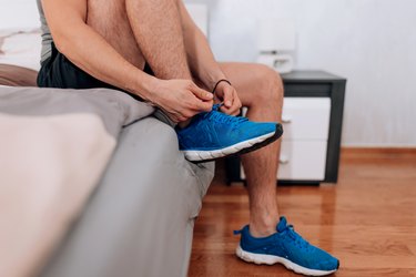 Close-up of person sitting on bed putting on running shoes in the morning.