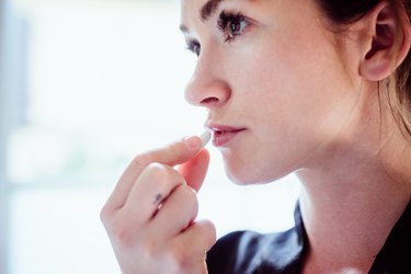 A close up photo of a person holding a white pill up to their lips showing overdosing on NSAIDs