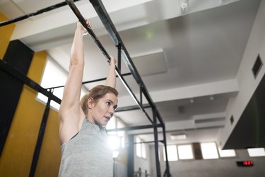 close up of a caucasian woman doing a dead hang exercise from a pull up bar in a gym