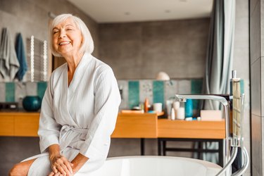 woman in white bathrobe getting into bathtub