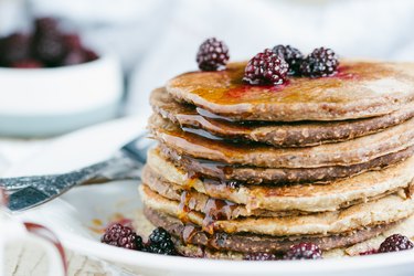 Whole wheat oatmeal pancakes stack on white plate with blackberries on top