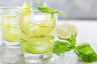 Refreshing summer homemade lemonade made from lime, lemon, cucumber and basil with ice in glass on old concrete background. Selective focus.