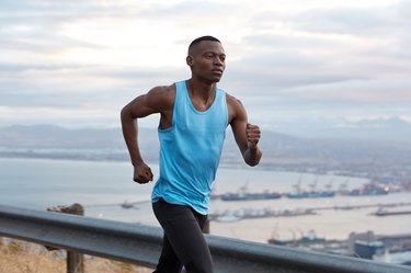 Outside shot of man running has goal achievement challenge to reach destination without break, works actively with hands, dressed in sportswear, joggs over nice nature view