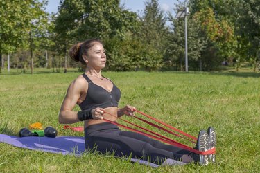 Athlete using long-loop resistance band to do row exercise while outside on yoga mat.