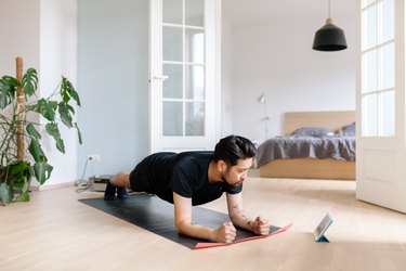 man doing forearm plank for core workout for constipation with tablet at home