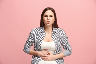 The stomach ache. The sad woman with stomach ache or pain on a pink studio background