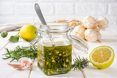 Fresh Italian Salad Dressing with Rosemary, Garlic and Lemon in a glass jar on wooden table next to raw ingredients.
