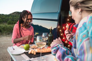 Multiracial happy friends celebrating and eating vegan food in front of camper van in park - Focus on black girl