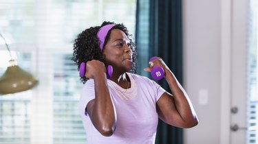closeup of a black middle-aged woman wearing purple doing zottman curls with purple 10 pound dumbbells