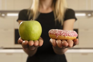 A woman holding an apple in one hand and a donut in the other