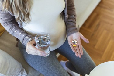 Cropped view of pregnant person with a handful of supplements, including vitamin B12
