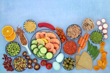 Healthy fruits, vegetables, and grains in bowls against a blue background