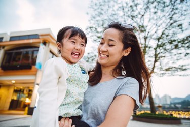 Mom holding toddler in park smiling, comfortable because she does strength exercises to help her carry her child