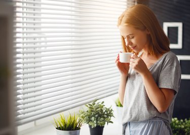 Happy young woman meets   morning with  cup of coffee  at   window