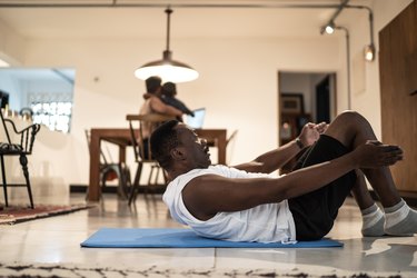 Person in white T-shirt and black shorts doing a sit-up at home in living room.