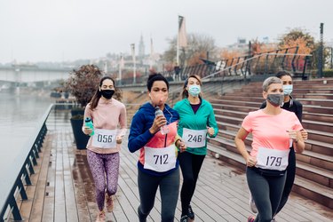 group of runners wearing masks and numbered bibs running a race on a pier