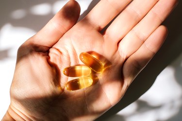 Woman's hand holding fish oil supplements on white background.