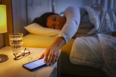 Woman in bed reaching mobile phone on night table
