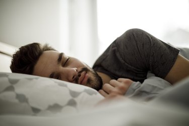 Young man sleeping in bed at home and using a sleep tracker