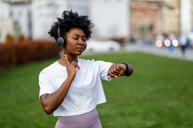A woman is checking her pulse at her neck after a workout outside