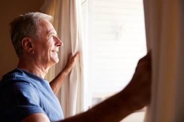 Smiling man opening the blackout blinds in his bedroom on a sunny morning