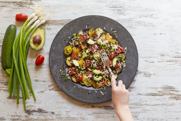 A child's hand holding a fork over a plate of vegetables on the kitchen table