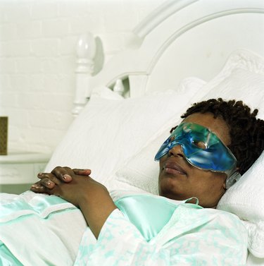 Woman lying in bed wearing an eye mask, one of the best natural remedies for pink eye