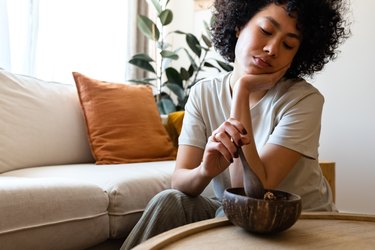 Young multiracial woman eating breakfast feeling very bored and unmotivated. Lack of appetite. Copy space.