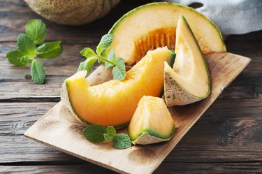 Slices of fresh, potassium-rich cantaloupe melon and sprigs of green mint on wooden cutting board