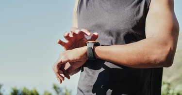 Person mit muskulösen Armen in einem dunklen Tanktop überprüft ihre Cardio -Zone auf der Uhr während eines Trainings