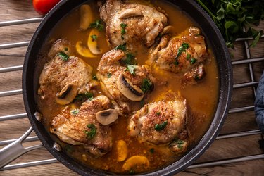 Top view of chicken thighs with bones cooked with mushrooms in a rich sauce, served in a pan.