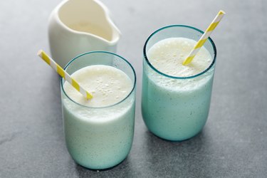 Two white liquid diet protein shakes in blue glasses with white pitcher in the background