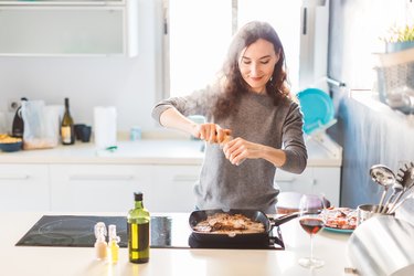 Young smiling woman cooking in the kitchen, adding spices to dish to help reduce inflammation