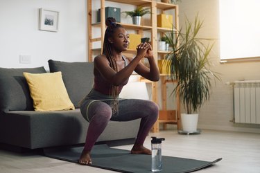 Person doing resistance band squat in living room on yoga mat.