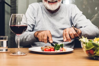 Older adult eating dinner at table with a glass of red wine