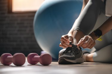 close view of a person tying their shoe next to a set of dumbbells, to represent building muscle