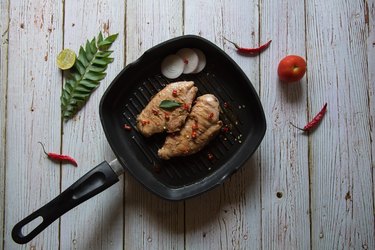 Top view of grilled chicken breast steak in a cooking pan along with condiments