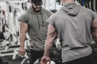 strong fitness sport athlete caucasian young man with beard wearing sportswear stretching his muscles during pause in workout training in gym club