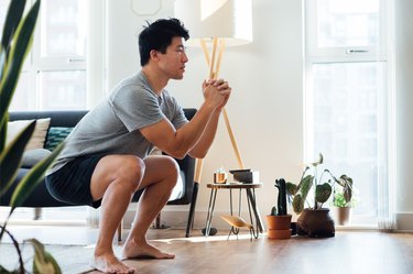Person in gray T-shirt and black shorts performing a deep squat in their living room