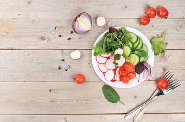 Green vegetable salad with cherry tomatoes, cucumber, radish and fresh arugula, detox diet. Healthy natural breakfast for weight loss, cholesterol and GMO free, selective focus, rustic style,