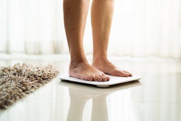 young woman standing on digital weight scale, to symbolize gaining weight but not belly fat