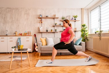 woman following an online workout and doing a split squat exercise in her living room