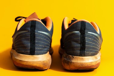 a rear view of a pair of old, dirty workout sneakers on a yellow background