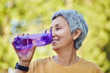 Close up mature woman holds plastic bottle drinking water