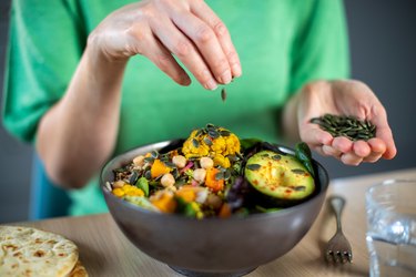 Close Up Of Woman Adding Pumpkin Seeds To Healthy Salad, as a natural remedy for restless legs syndrome relief